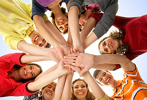 A group of young adults stacking their open hands to imply teamwork.